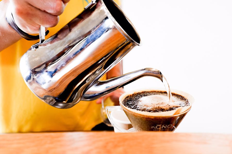 Person pouring water from a kettle into a cup of ground coffee