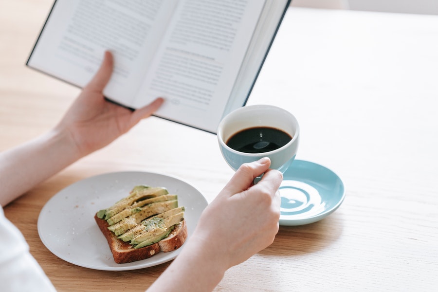 Person reading a book with a snack and a coffee