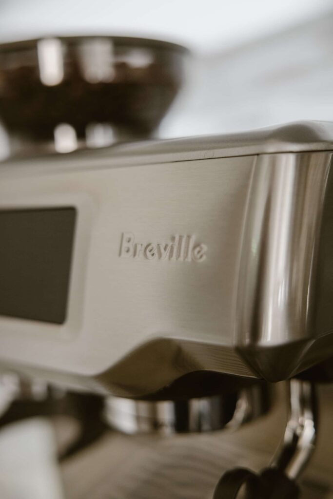 A silver Breville espresso machine with coffee beans in the bean hopper in the kitchen