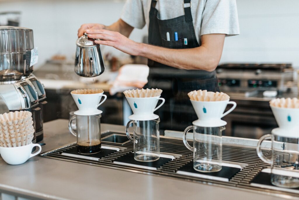 A barista pours fresh coffee on white coffee mugs with a brown coffee filter in a coffee shop