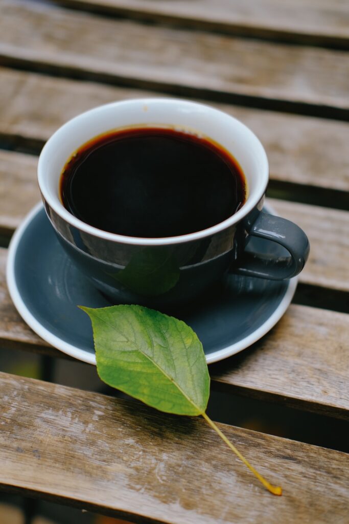 Black coffee in a green cup placed on a green saucer beside a green leaf on a brown wooden table